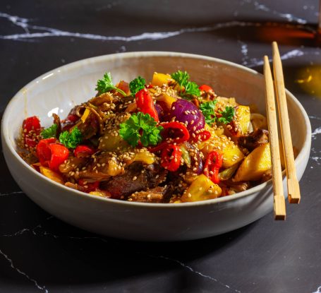 Bunt gefüllte Schüssel mit Gemüse, Fleisch und frischen Kräutern, serviert mit Essstäbchen