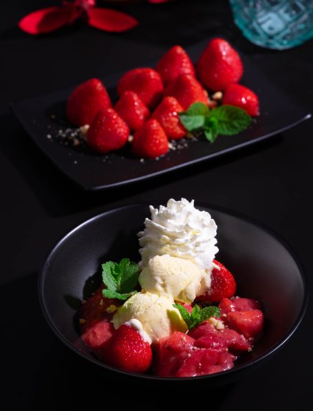 Erdbeeren und Rhabarberkompottserviert mit Sahne und Vanilleeis in einer schwarzen Schüssel.