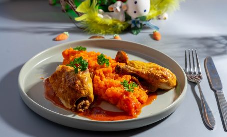 Hühnchenschenkel mit Möhrenpüree und Petersilie auf einem grauen Teller.