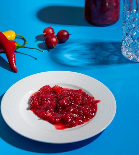 Stachelbeeren Chutney auf einem weißen Teller, umgeben von frischen Chilis und Stachelbeeren.